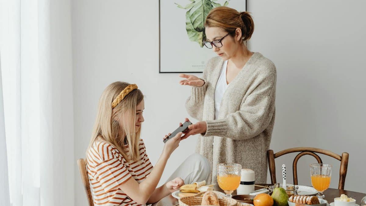A mother and daughter in a discussion over phone use during breakfast at home.