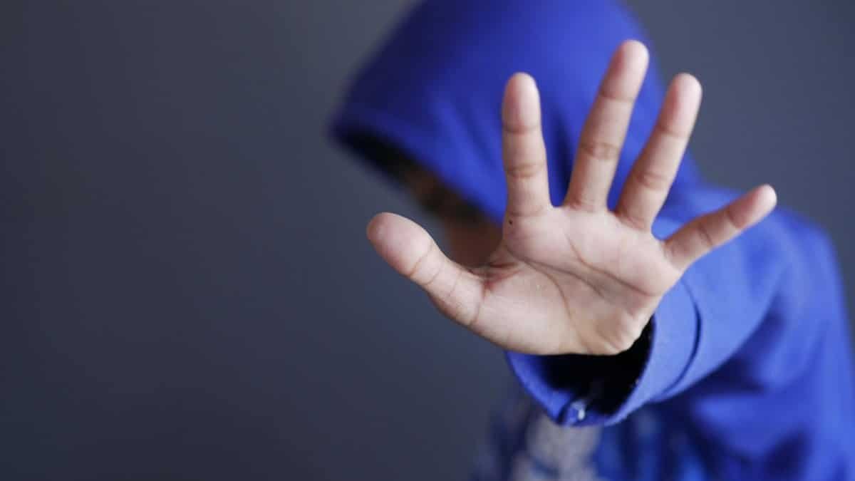 Close-up of a child in a blue hoodie holding up a hand. Blurred background and selective focus.