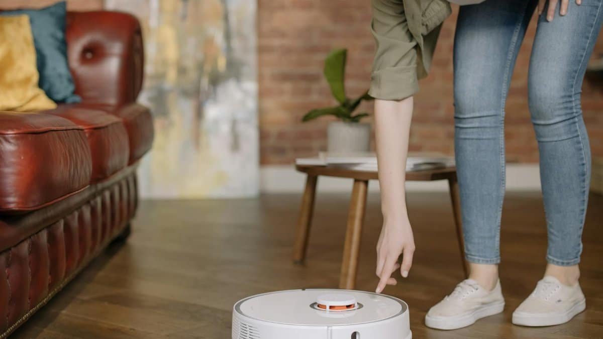A woman in jeans interacts with a robotic vacuum cleaner in a cozy, stylish living room.