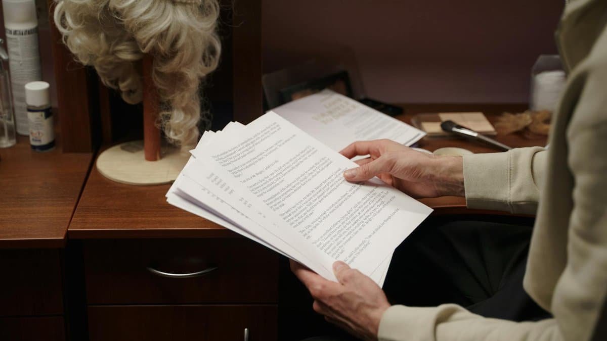 An actor reviews a script in a backstage dressing room, preparing for a theater rehearsal.