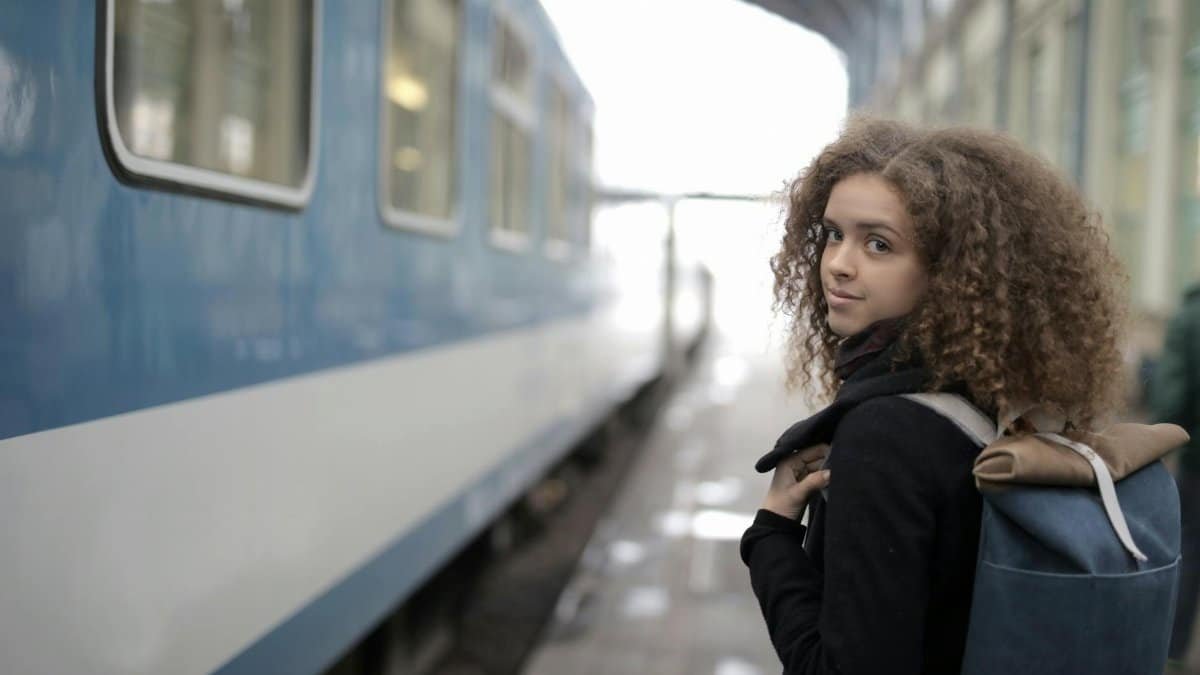 Young woman with backpack looking over shoulder at train station, ready for adventure.