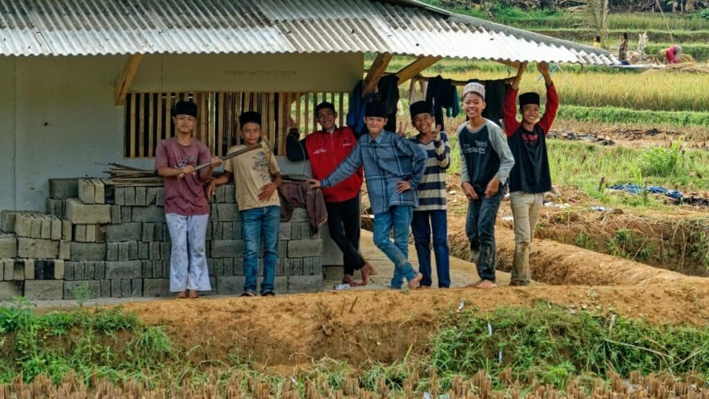 A cheerful group of boys posing near a rural structure in Indonesian farmland.