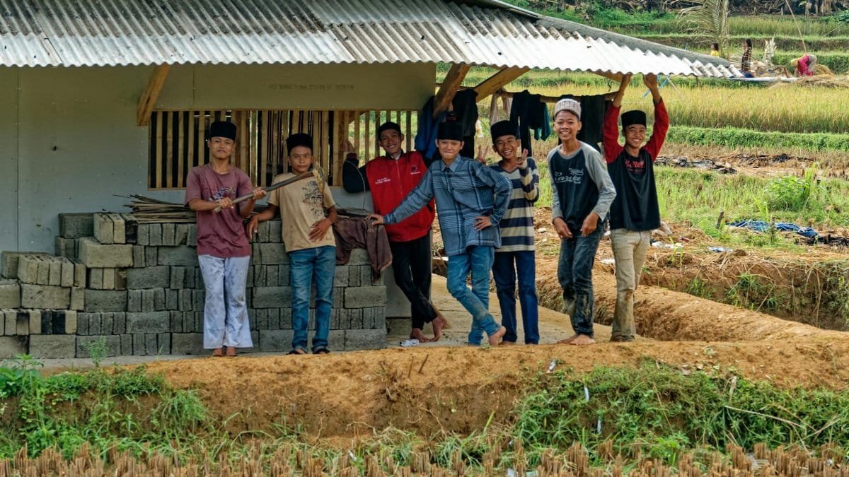 A cheerful group of boys posing near a rural structure in Indonesian farmland.