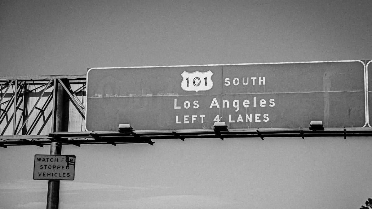 Monochrome image of Route 101 highway sign leading to Los Angeles, highlighting four lanes.