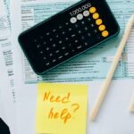 Top view of financial papers with a calculator, pencils, and a note saying 'Need help?' indicating tax or accounting assistance.