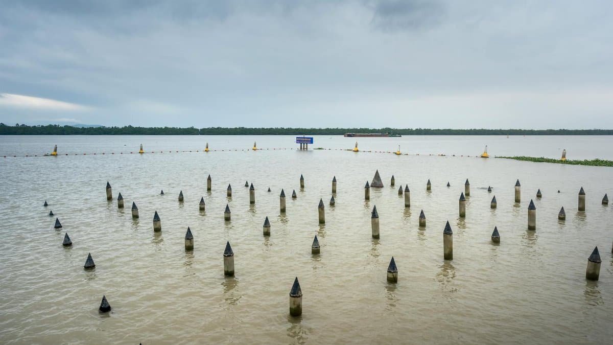 Tranquil view of the Bach Dang River featuring traditional wooden stakes against a cloudy sky.