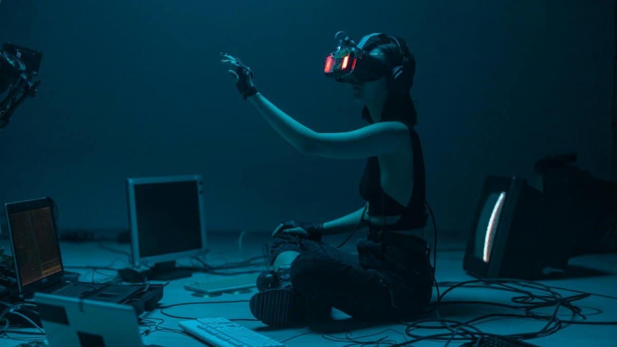Woman immersed in virtual reality, surrounded by tech, in a dimly lit room.