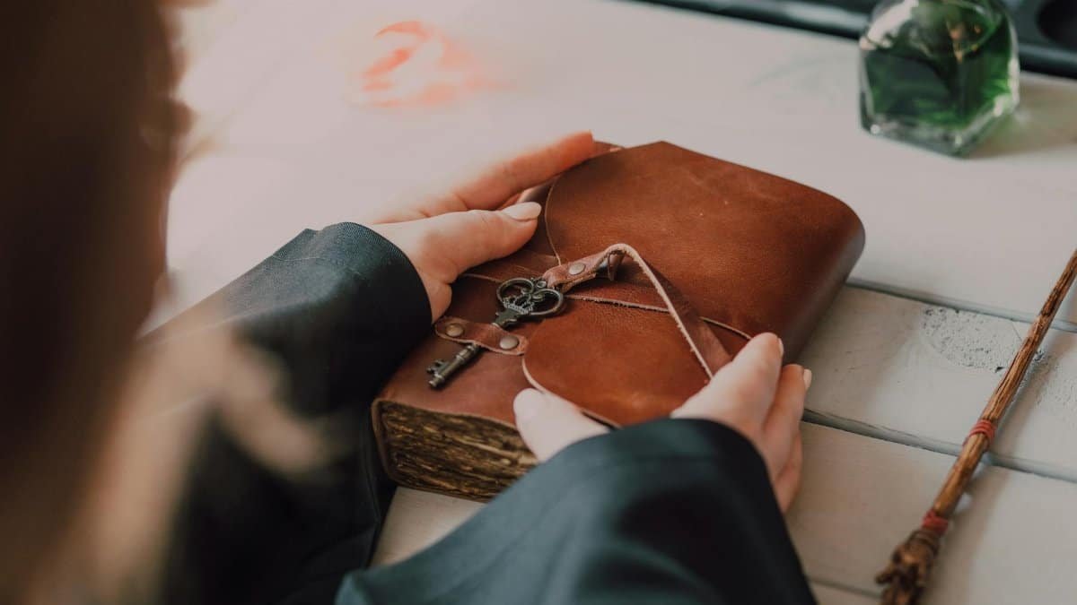 Hands hold a leather book with key on it, surrounded by magic wand and potion.