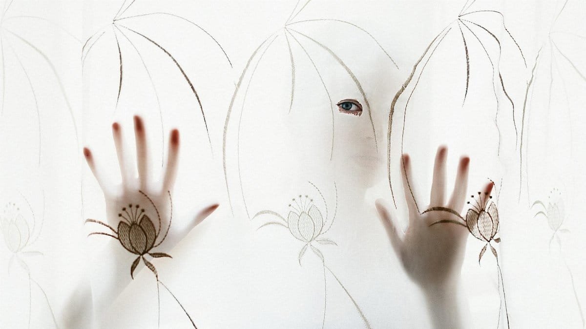 Artistic silhouette of a person with hands and eye visible through a decorative curtain.