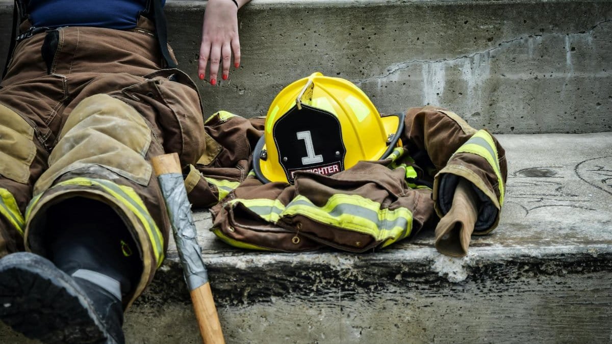 Firewoman taking a break on concrete steps with gear and helmet nearby.