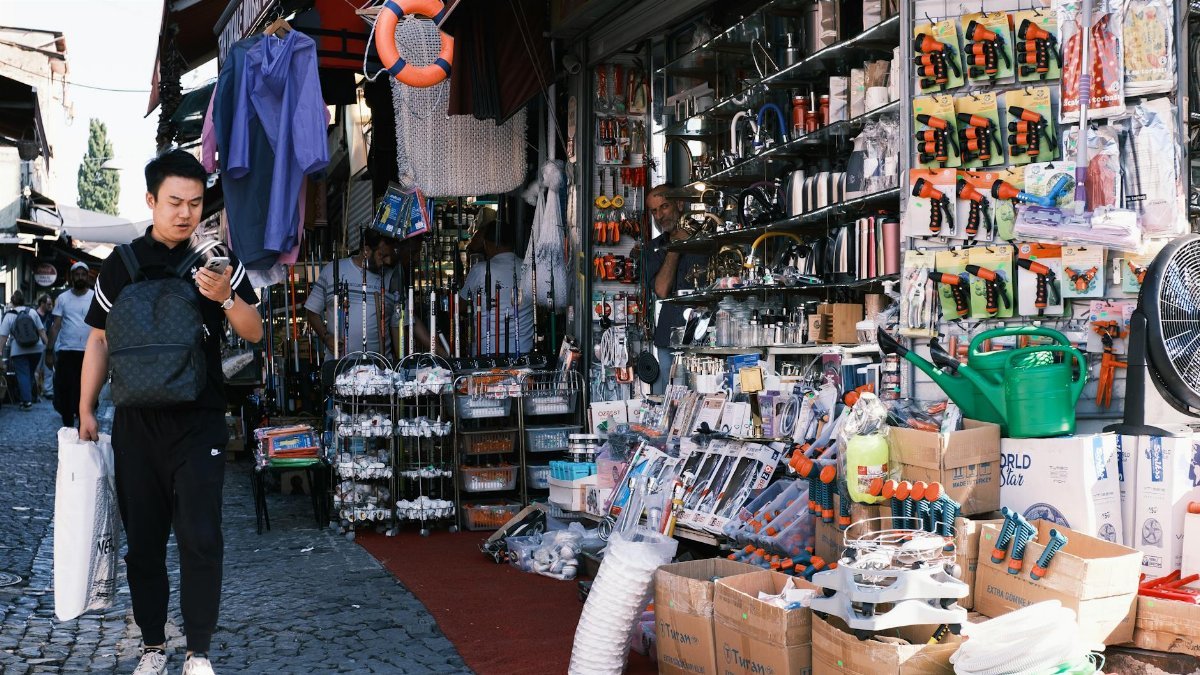 Man browsing tools at a vibrant outdoor market stall offering diverse hardware products.
