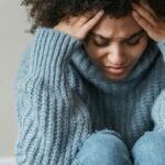 Young woman with curly hair looks thoughtful and pensive, wearing a cozy sweater indoors.