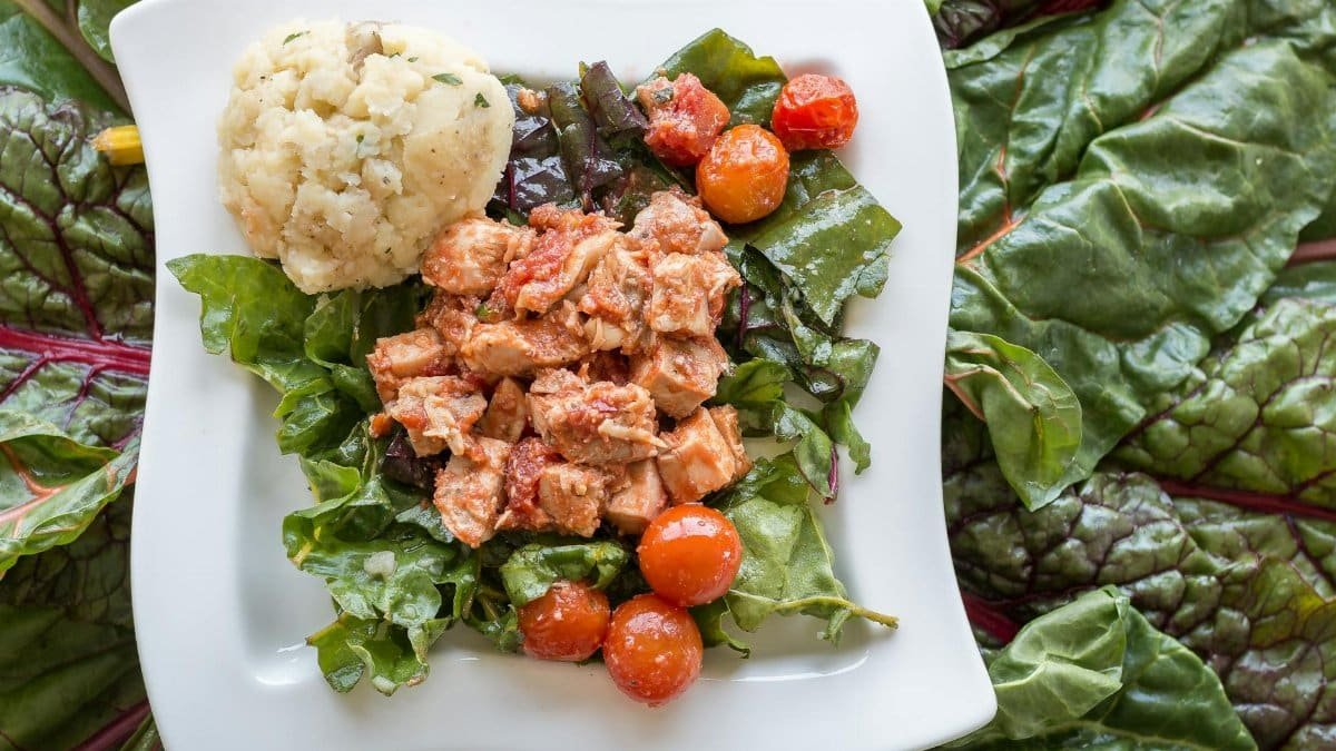A nutritious dish featuring fish, tomatoes, and greens paired with mashed potatoes served on an elegant plate.