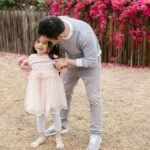 A father shares a joyful moment with his daughter in a blooming garden with vibrant flowers.
