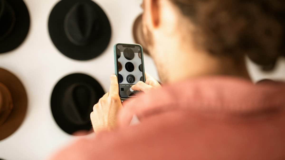 A person takes a photo of a hat display with a smartphone. Modern fashion concept.
