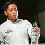 A bartender presents a bottle of Tequila 30-30 in a restaurant environment.
