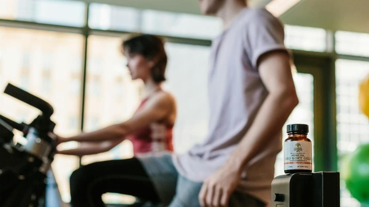 CBD gel bottle in gym with exercising adults, suggesting health benefits.