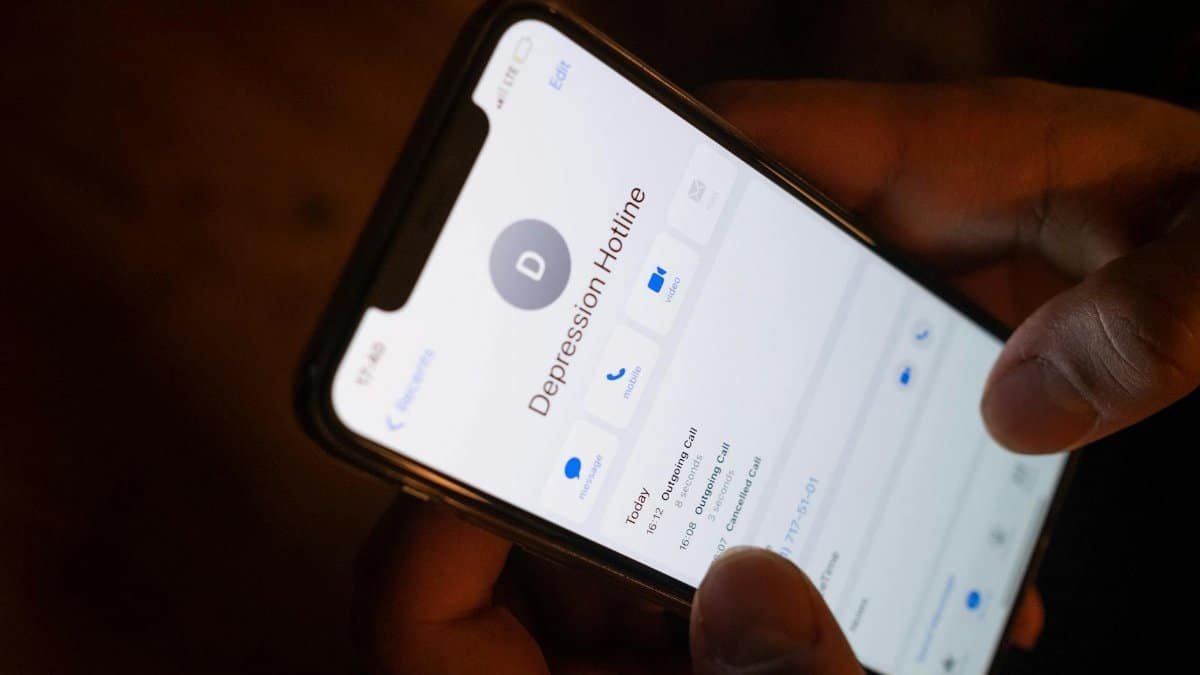 A close-up of a hand holding a smartphone displaying a depression hotline contact.