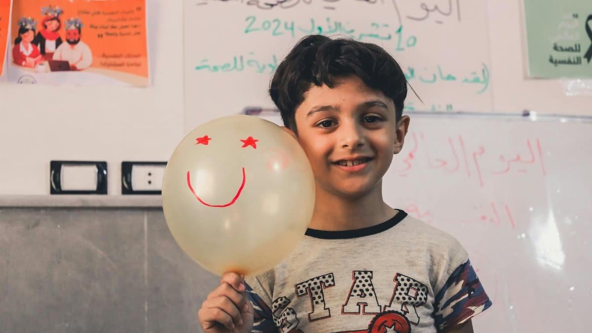 Child holding a smiley balloon, promoting mental health awareness in a classroom setting.