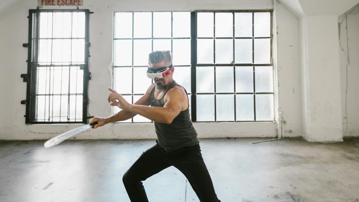 Man with VR headset practicing virtual sword fighting in an industrial-style loft studio. Futuristic workout concept.