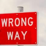 Clear image of a bright red 'Wrong Way' traffic sign against a cloudy sky in Miami, Florida.