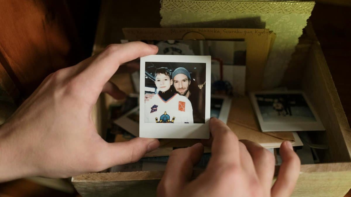 Close-up of hands holding a nostalgic Polaroid photo of father and son from a memory box.