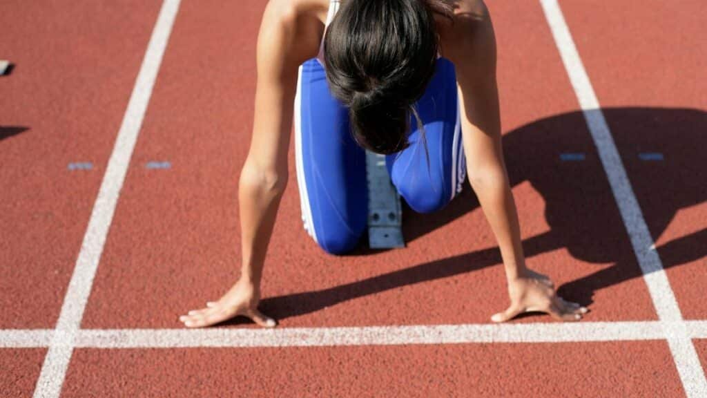 A female athlete crouches at the starting line, ready to sprint on a sunny day.