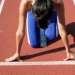 A female athlete crouches at the starting line, ready to sprint on a sunny day.