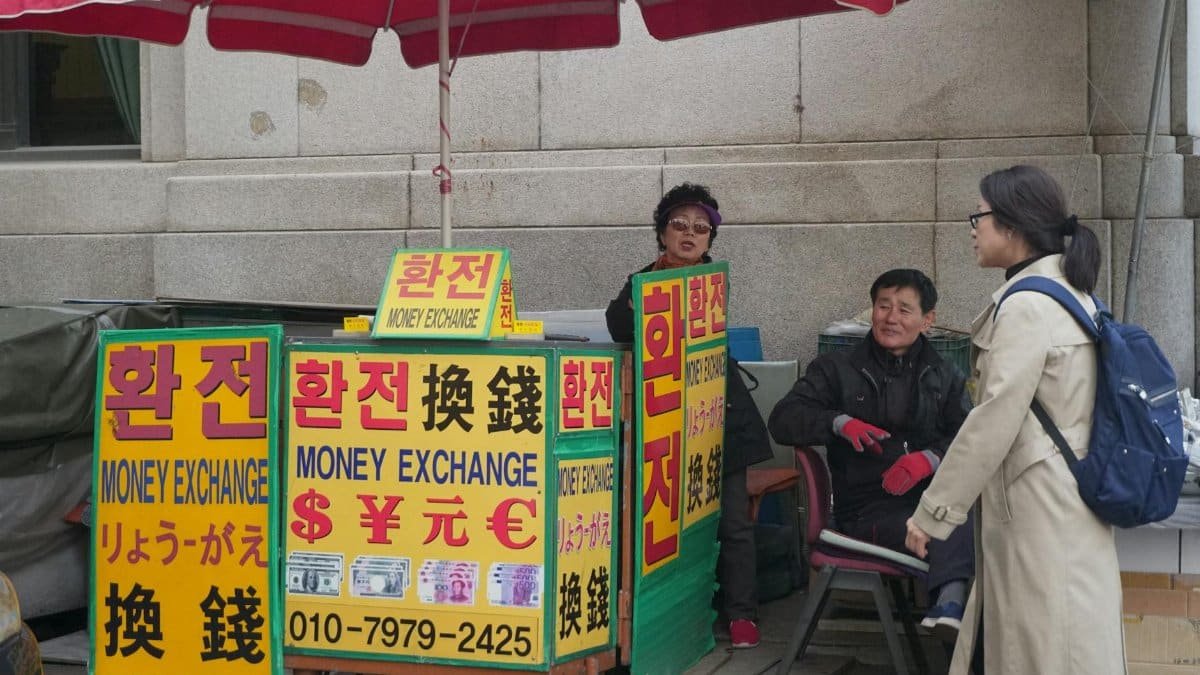 Two adults conversing at an outdoor money exchange booth with vivid signage in a city street.
