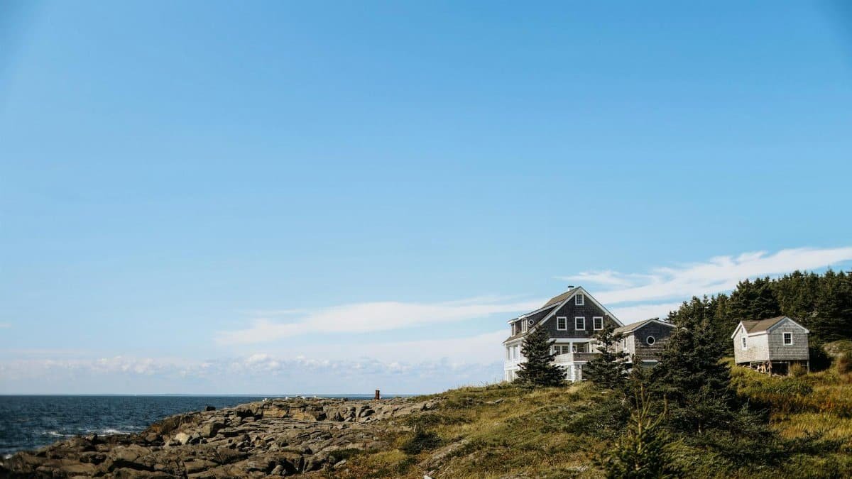 Charming houses overlooking a rocky shore on Monhegan Island with a clear blue sky backdrop.