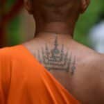 Thoughtful moment of a tattooed monk amidst spirituality in Bangkok temple.