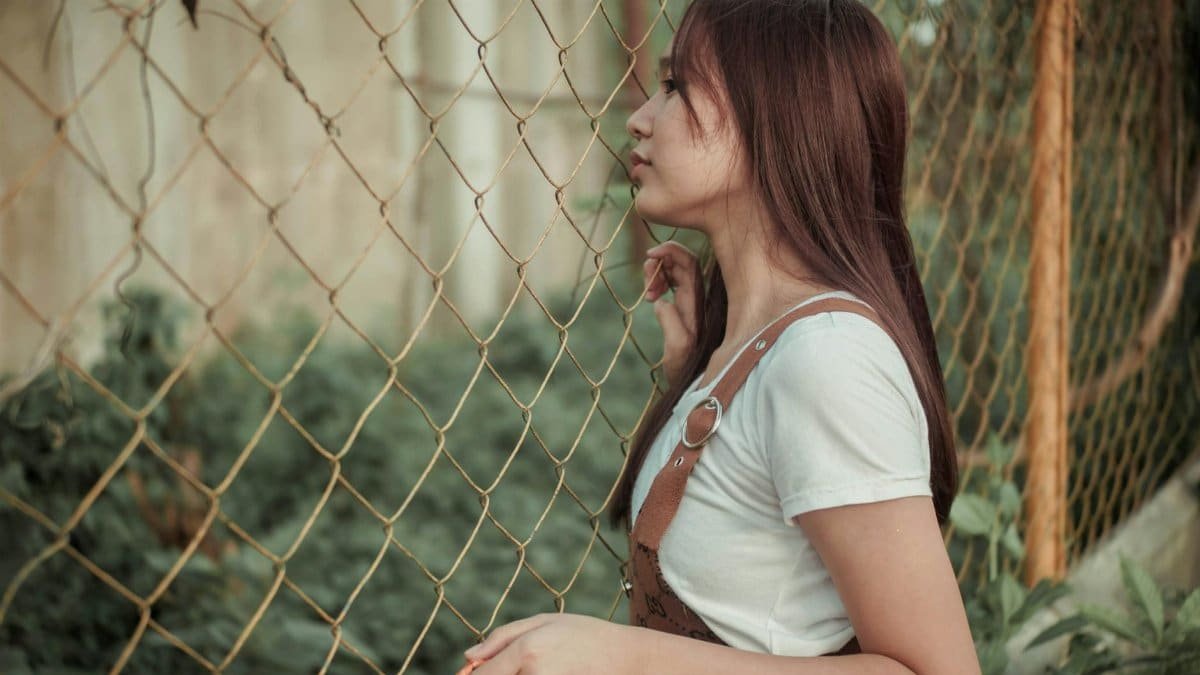 Side view of young female thinking on escape while standing near fence in countryside