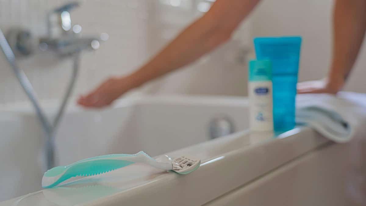 Close-up of shaving razor on bathtub edge with faucet in background, illustrating personal grooming.