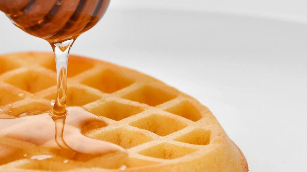 Close-up of a waffle being drizzled with honey, showcasing texture and sweetness.