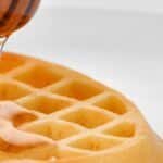 Close-up of a waffle being drizzled with honey, showcasing texture and sweetness.