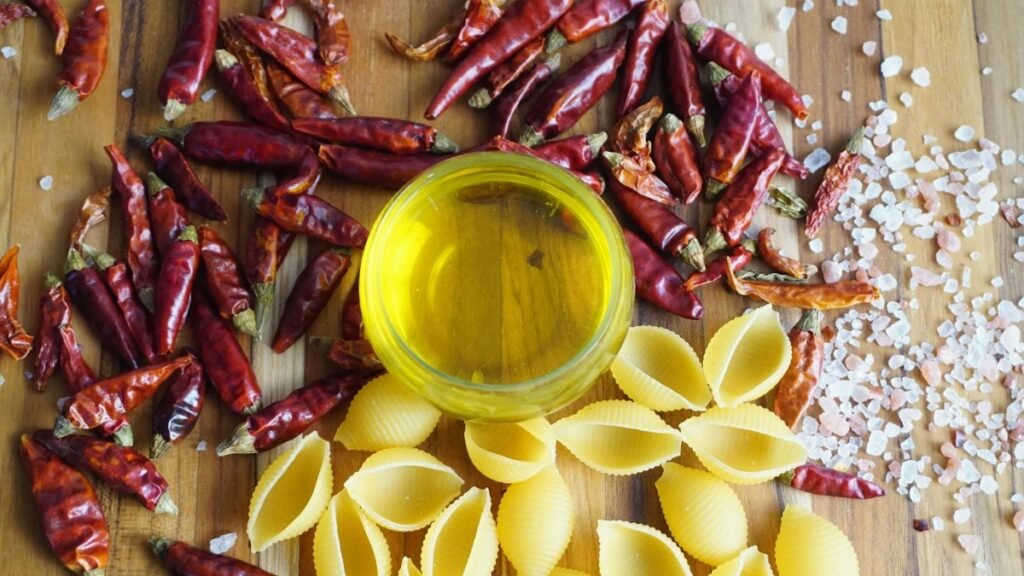 A vibrant display of chili peppers, pasta, and olive oil on a wooden board.