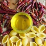 A vibrant display of chili peppers, pasta, and olive oil on a wooden board.
