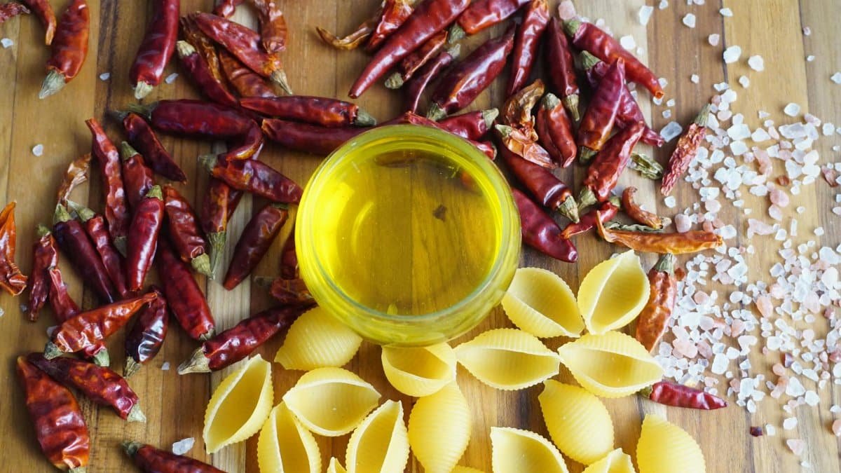 A vibrant display of chili peppers, pasta, and olive oil on a wooden board.