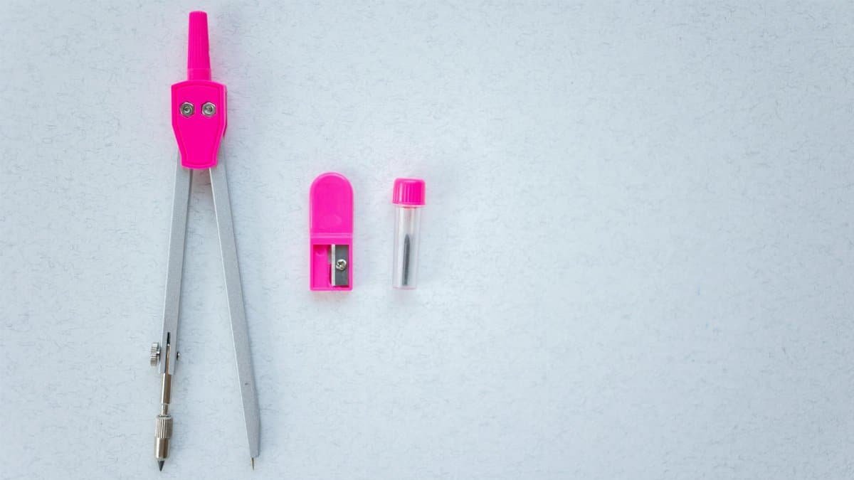 A close-up of a pink drawing compass, sharpener, and lead tube on a white surface.