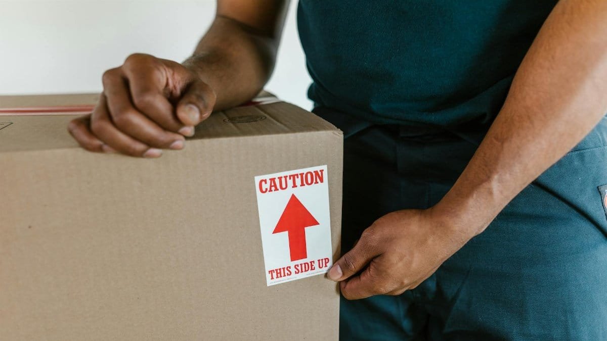 A person handling a moving box with a 'caution this side up' label indoors.