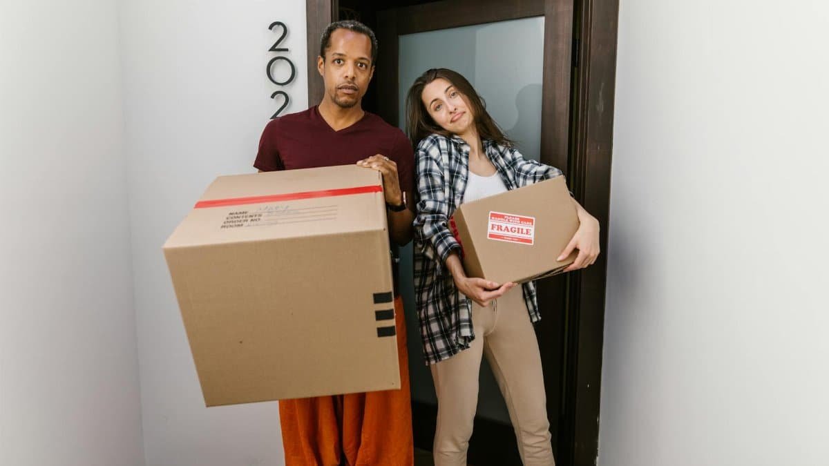 A couple carrying moving boxes indoors, settling into their new apartment.