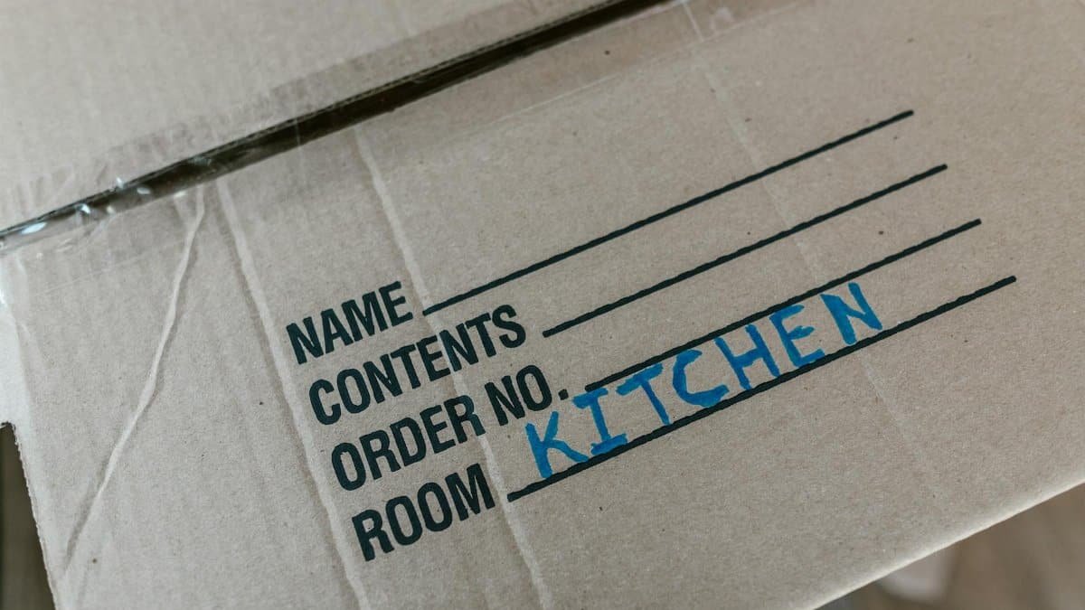 Cardboard box labeled with room destination for kitchen during moving process.