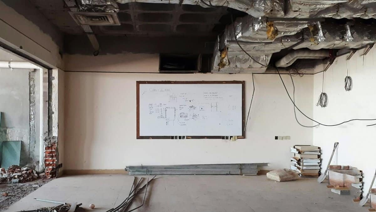 An empty room under construction with exposed ceiling ducts and a whiteboard.