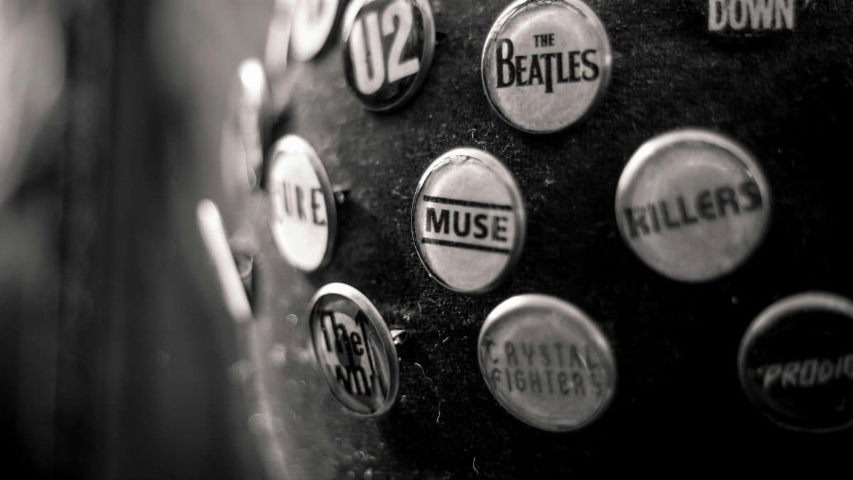 Close-up of vintage music band pins on black fabric, showcasing iconic rock band logos.