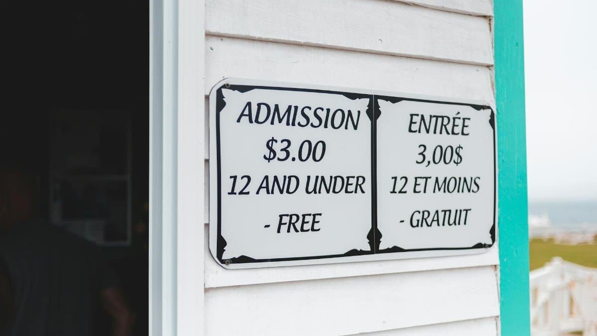 Bilingual sign displaying admission prices in English and French at building entrance.