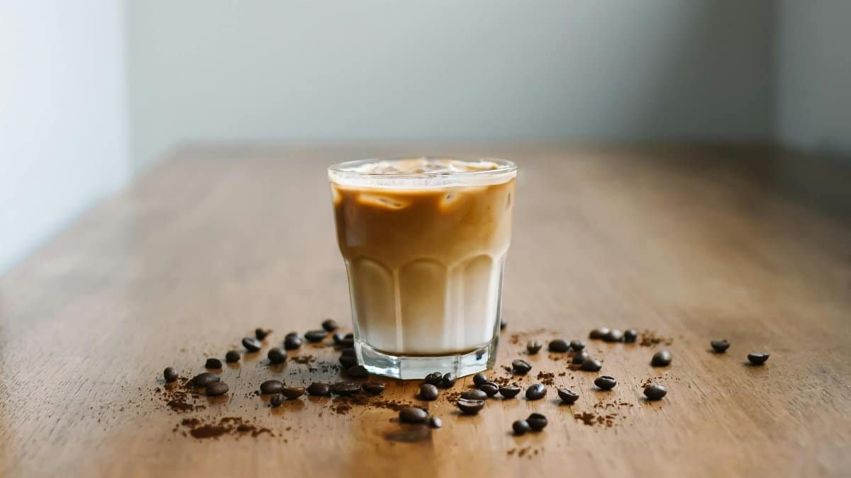 Refreshing iced latte with coffee beans on a wooden table surface.