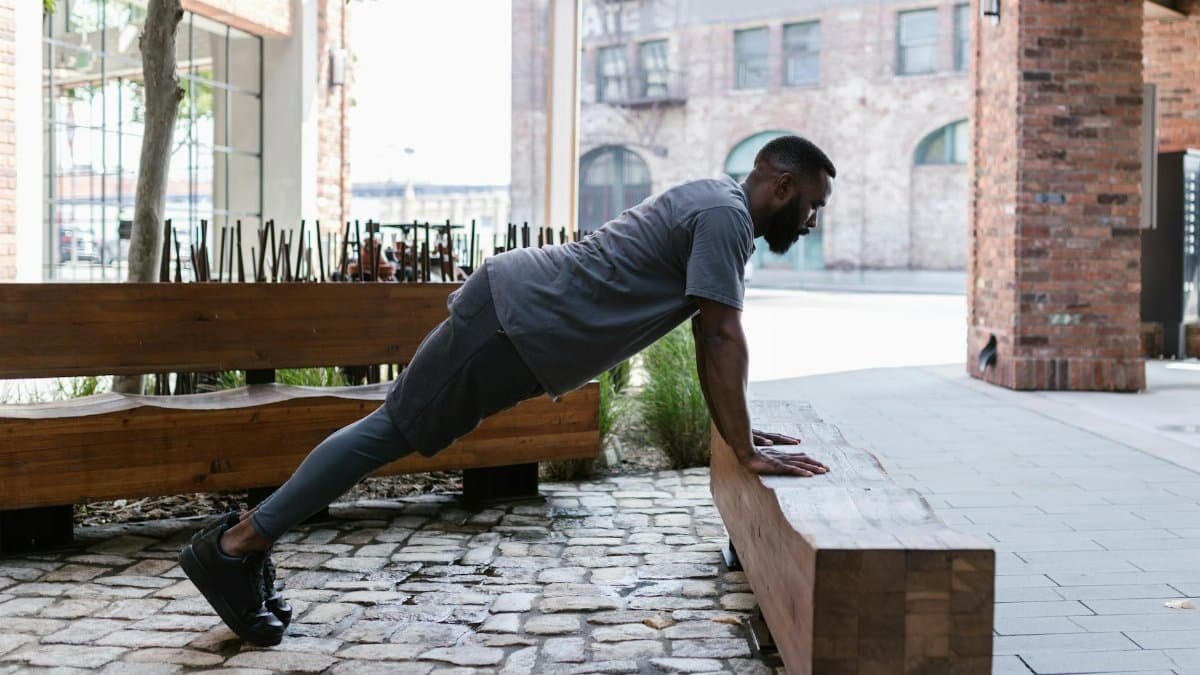 African American man performing push-ups outdoors in an urban setting, showcasing strength and fitness.