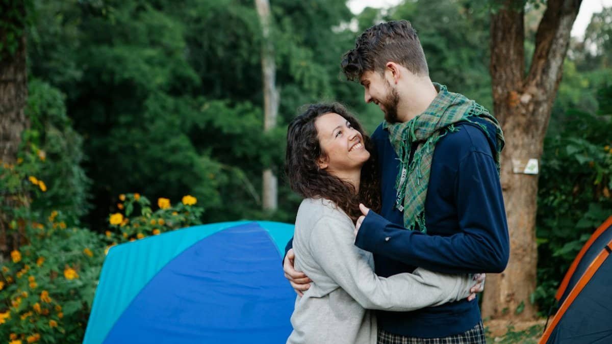 Happy couple sharing a loving embrace at a campsite in a lush green forest, filled with warmth and affection.