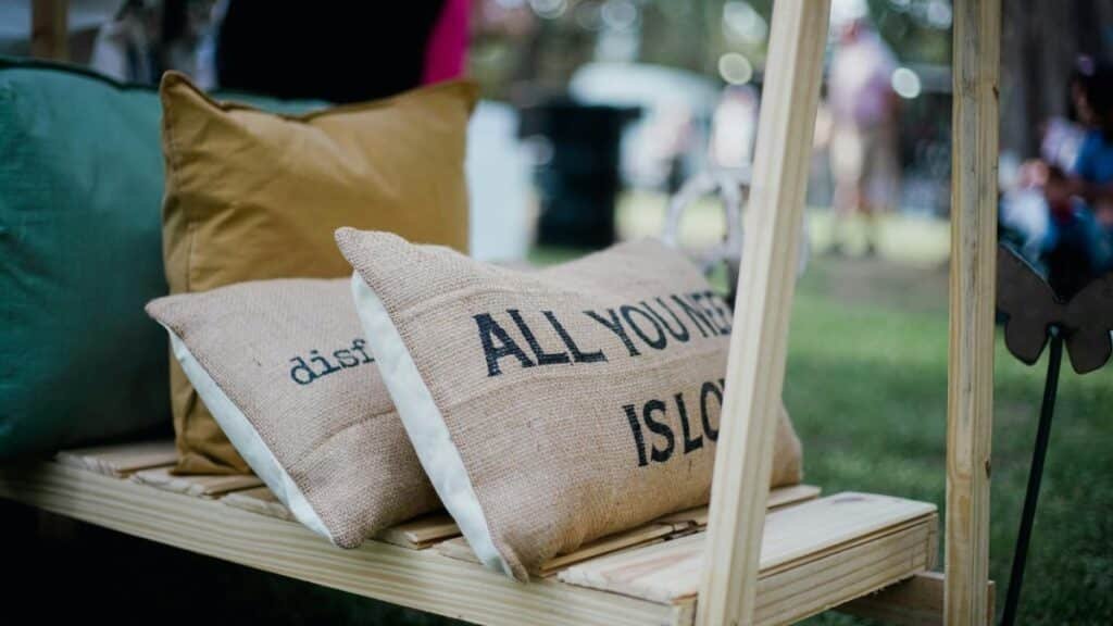 Outdoor cushions display with 'All You Need Is Love' slogan on burlap texture.