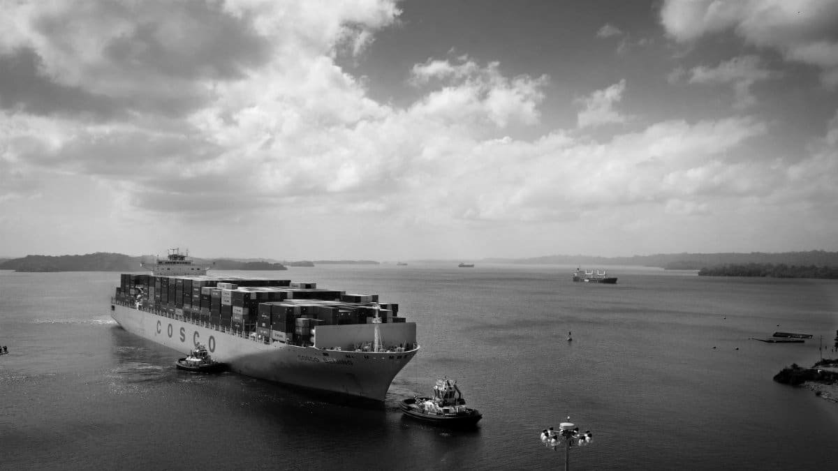 Black and white image of a large container ship navigating through calm waters.